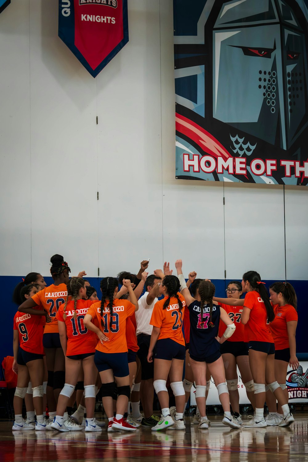 a group of girls in orange and blue uniforms standing on a basketball court