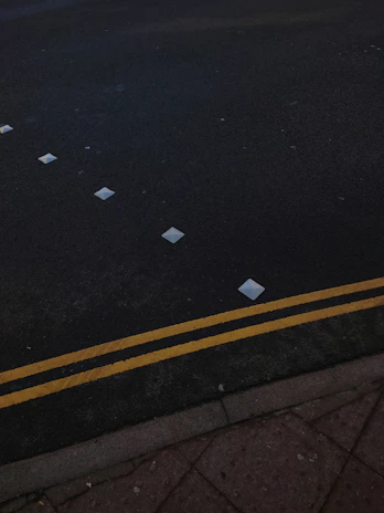 Workers installing reflective road studs along a curved highway at dusk with safety gear and machinery.