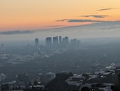 A stylish cityscape at dusk with a subtle overlay of perfume mist drifting through the air.