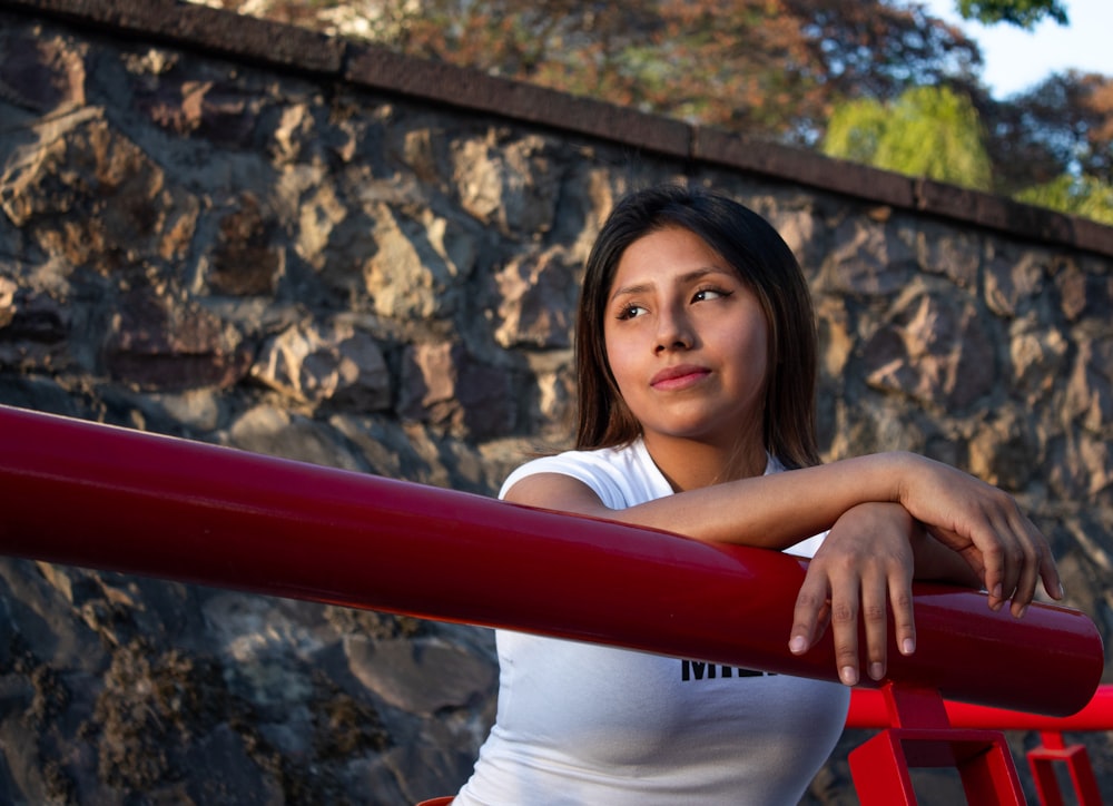 a woman leaning on a red railing in front of a stone wall