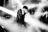 A blurred black and white image capturing the movement and energy of a musician performing on stage. Bright stage lights create dynamic lines across the scene, adding to the sense of motion.