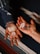 Two hands are holding a collection of crystals of various shapes and colors, positioned above a textured, multicolored fabric. The left hand, adorned with a beaded bracelet and rings, holds larger, white crystals, while the right hand holds smaller, varied stones.