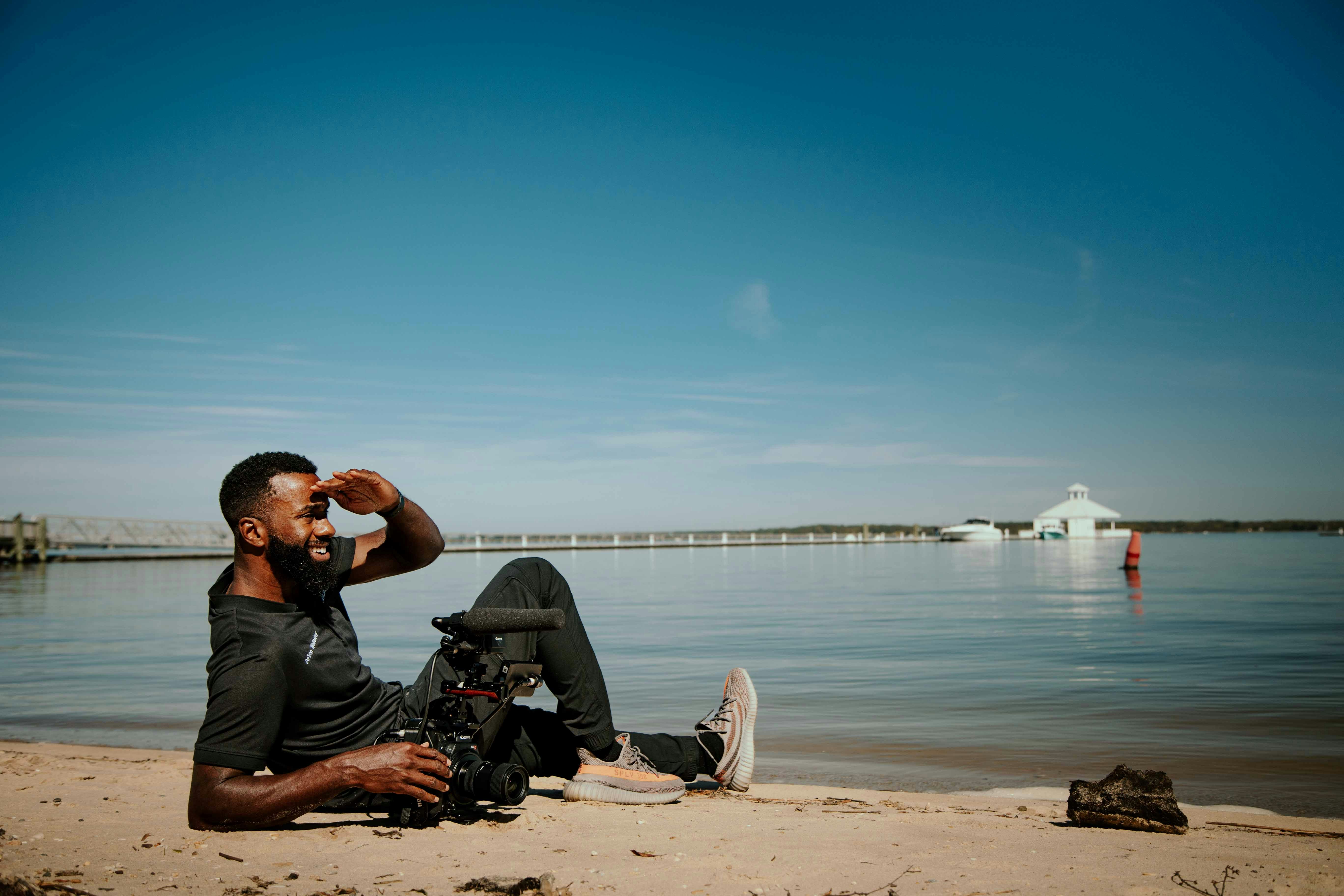 a man sitting on a beach next to a body of water