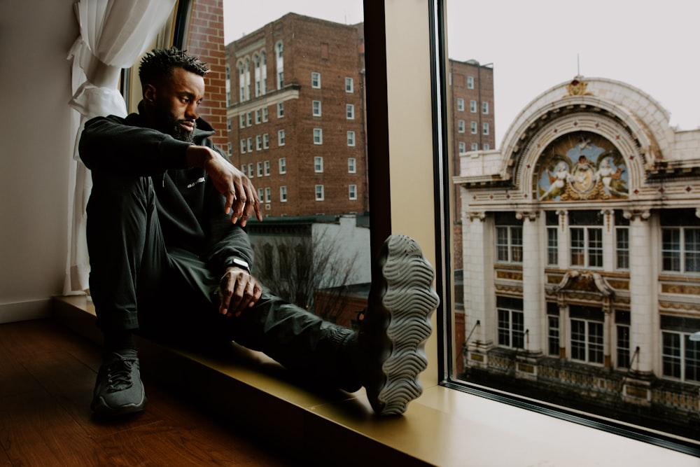 a man sitting on a window sill looking out the window