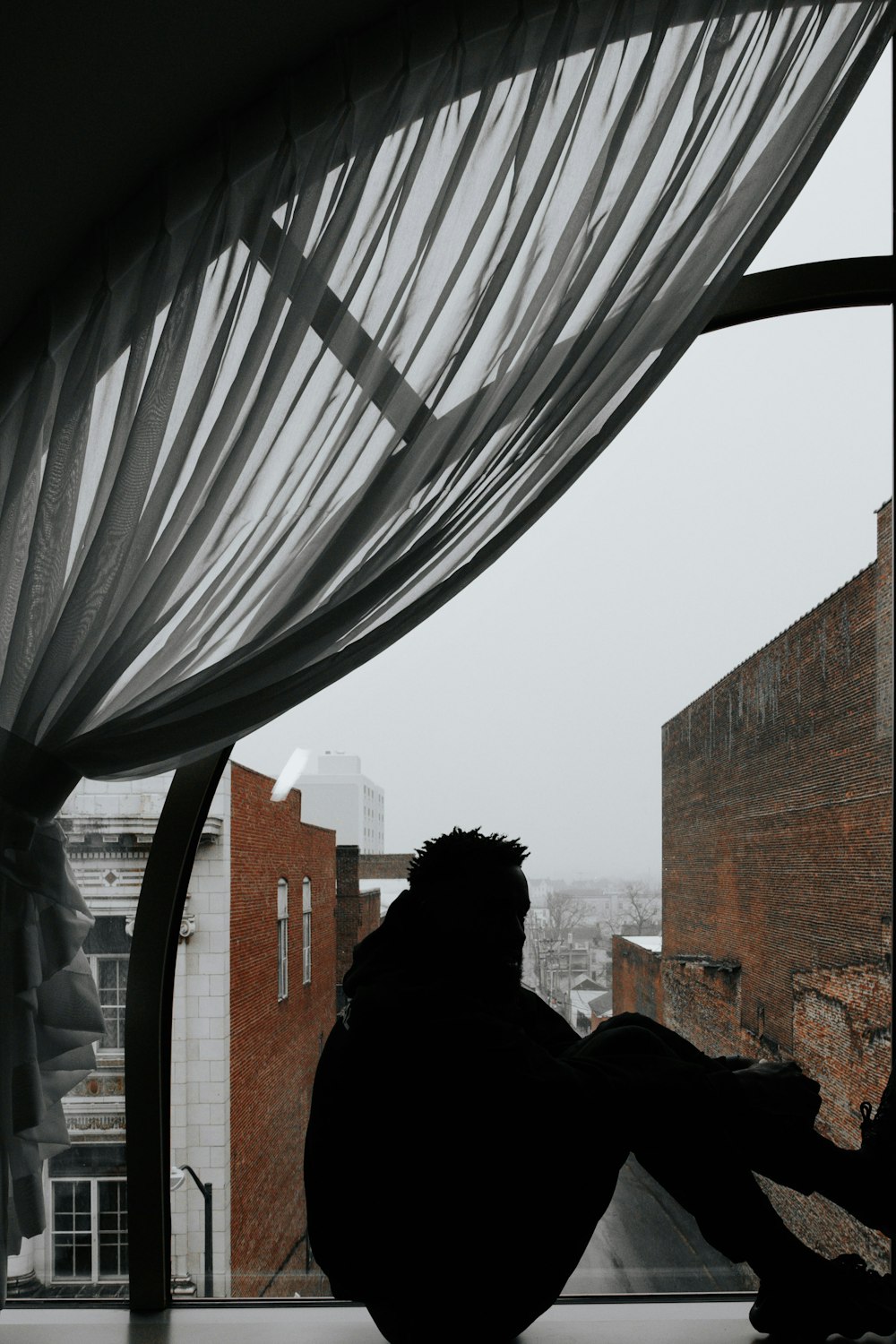 a person sitting on a window sill looking out at a city