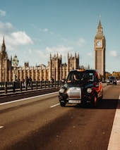 A sleek taxi cruising past iconic London landmarks under a cloudy sky.