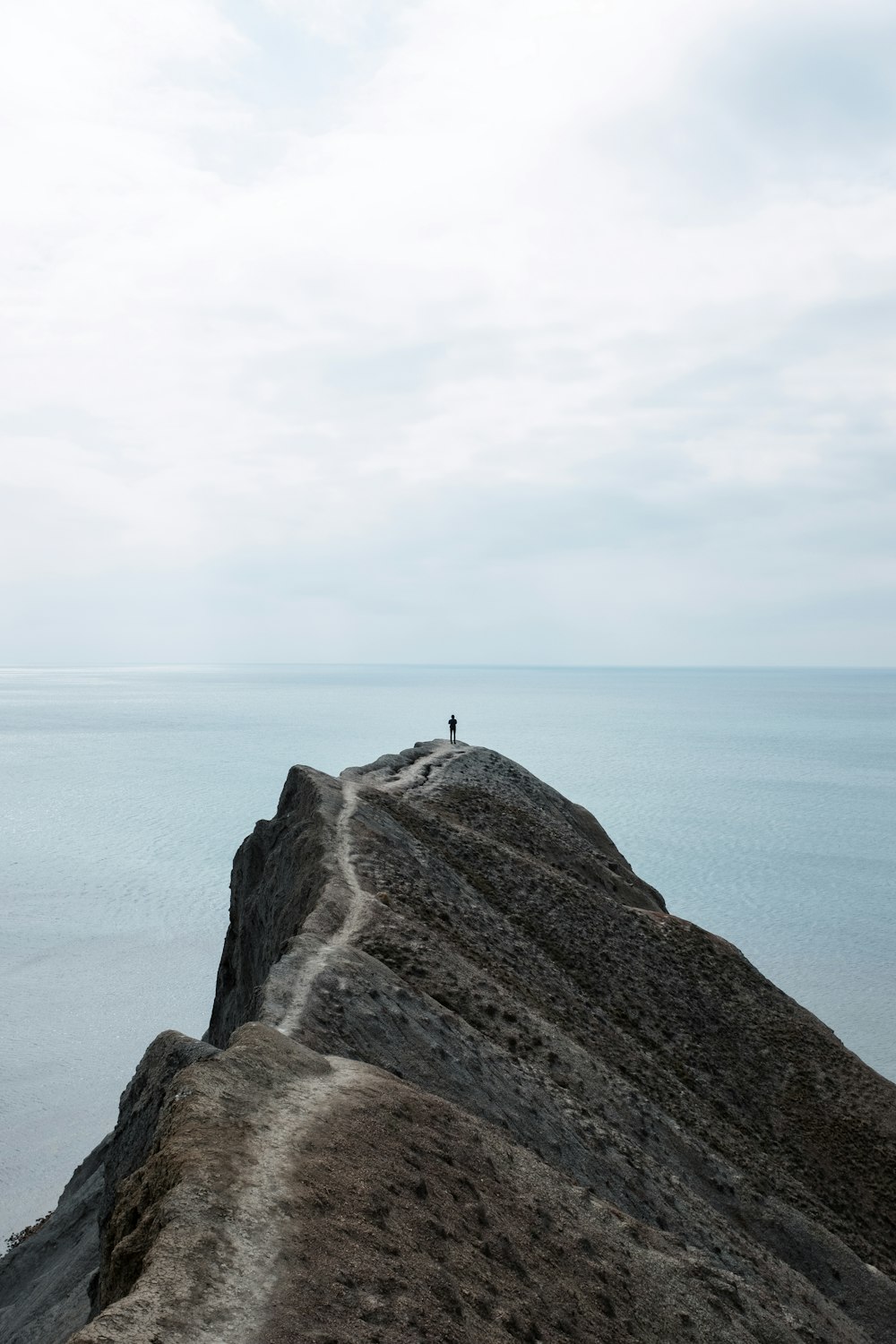 a person standing on top of a mountain next to the ocean