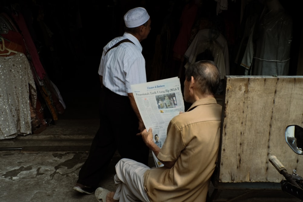 a man sitting on the ground reading a newspaper