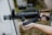A person holding a tactical weapon with a cylindrical barrel and attached scope, standing outdoors. The weapon is predominantly black with a textured surface and appears to be designed for military or law enforcement use.