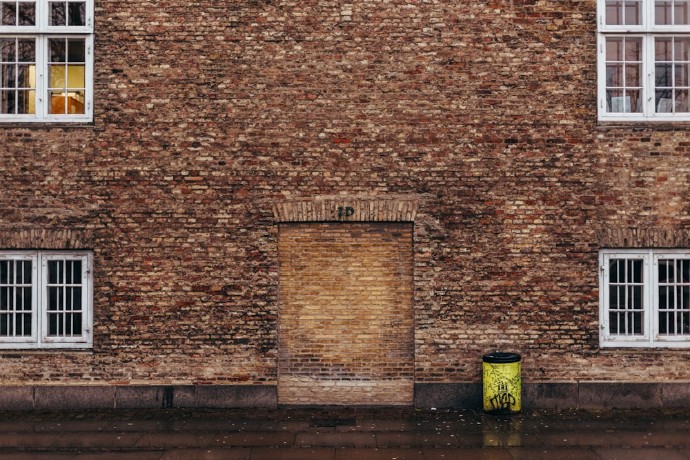 un edificio di mattoni con un bidone della spazzatura giallo di fronte