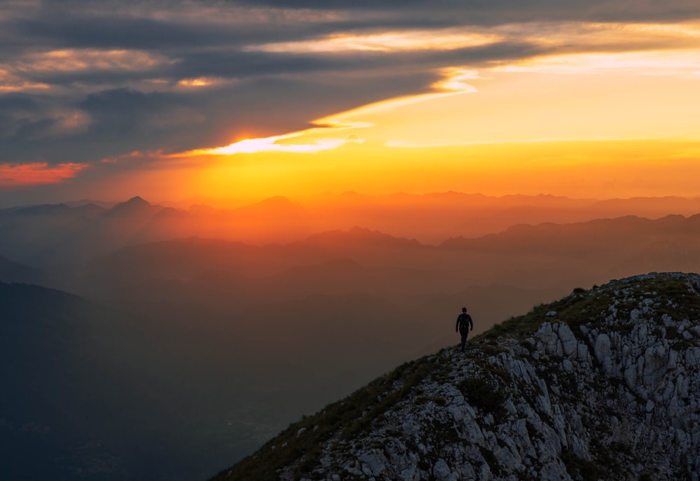 une personne debout au sommet d’une montagne au coucher du soleil