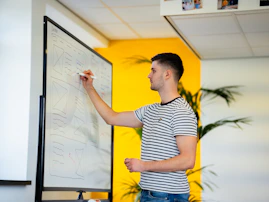 a man standing in front of a whiteboard writing on it
