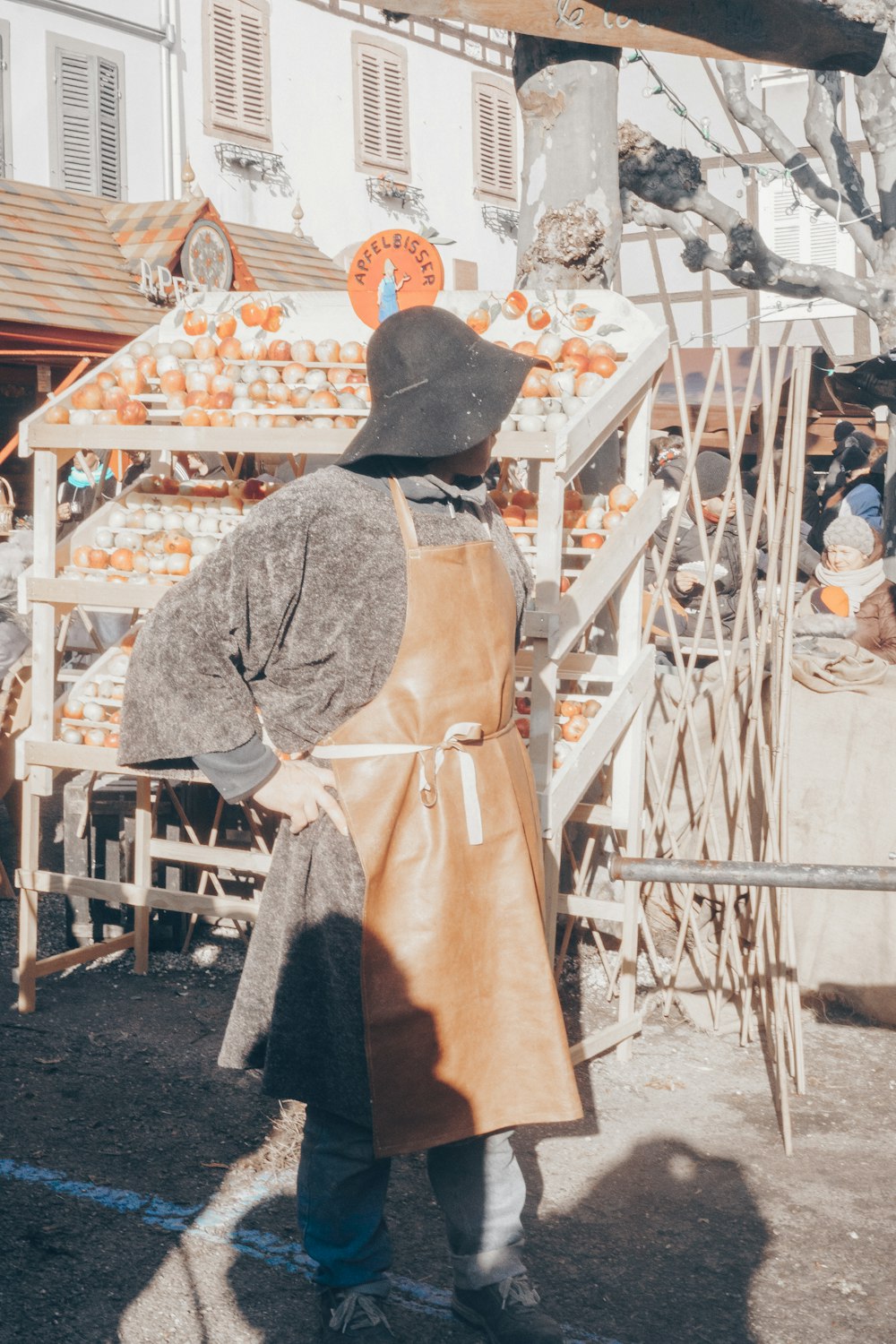 un homme en tablier et chapeau debout devant un stand de citrouilles