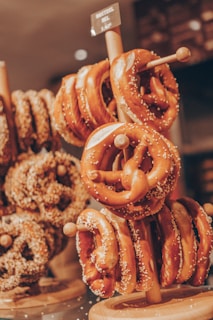 A display rack holds several freshly baked pretzels adorned with salt. In the background, more pretzels and bread rolls can be seen, adding to the bakery setting. The warm lighting gives the pretzels an inviting appearance.
