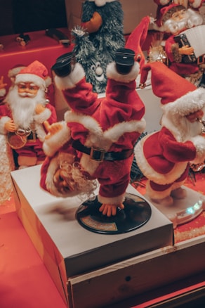Several Santa Claus figures are displayed, with one performing a headstand on a rotating base. The Santas are dressed in traditional red suits with white fur trim, surrounded by festive decorations including a bearded figure in the background holding an accordion.