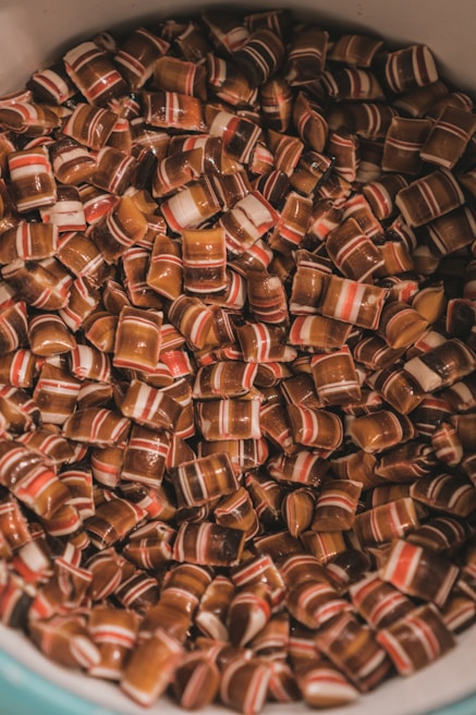 A collection of small, rectangular candies with striped patterns in shades of brown, white, and red fills the container. The candies are glossy and appear to have a hard texture.