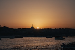 MG TURIZM Golden hour over the Bosphorus with silhouettes of mosques and boats.