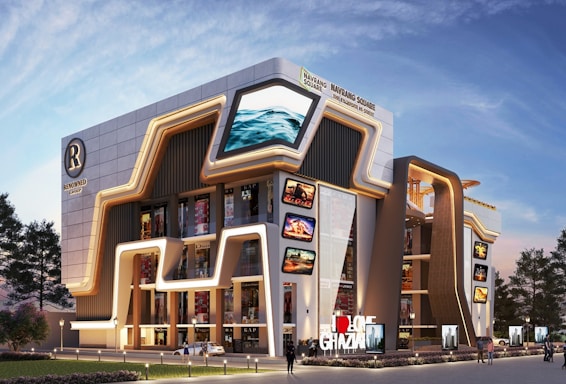 A modern, architecturally unique building featuring futuristic design elements with illuminated signage and advertisements. The facade includes large digital screens displaying various images and videos. Surrounding the structure are landscaped areas with trees and streetlights.