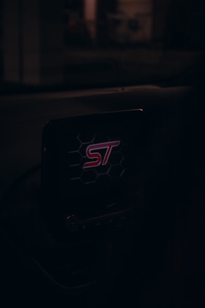 A car dashboard with a screen displaying the logo 'ST' surrounded by a hexagonal pattern, illuminated in a dark environment.