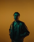 A close-up of a model wearing a sleek black leather jacket with gold accents under soft lighting.