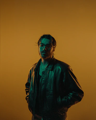 A stylish model wearing a rugged leather jacket against a dark emerald green backdrop with gold accents.