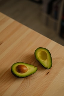 A fresh green avocado sliced open on a white wooden table, symbolizing healthy keto fats.