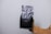 A hand is holding a black, matte-finish, resealable pouch against a plain white background. The pouch is smooth and simple, indicating it may be used for packaging food or other products.