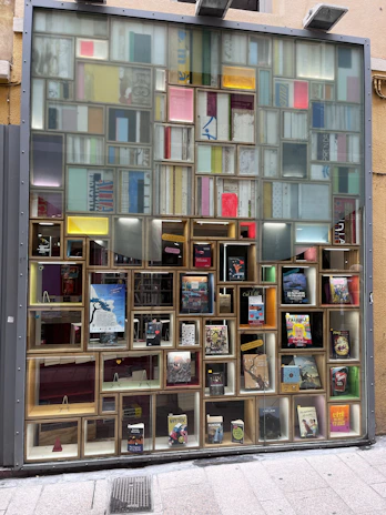 A bright, inviting storefront window displaying art pieces and books under the aion.gemini brand