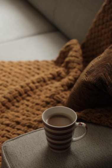 A cozy living room corner with a warm armchair, soft throw blanket, and a steaming cup of tea on a small wooden table.