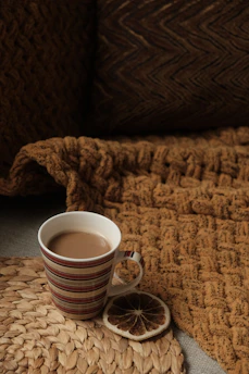 A cozy ceramic mug filled with steaming coffee, resting on a soft knitted blanket.