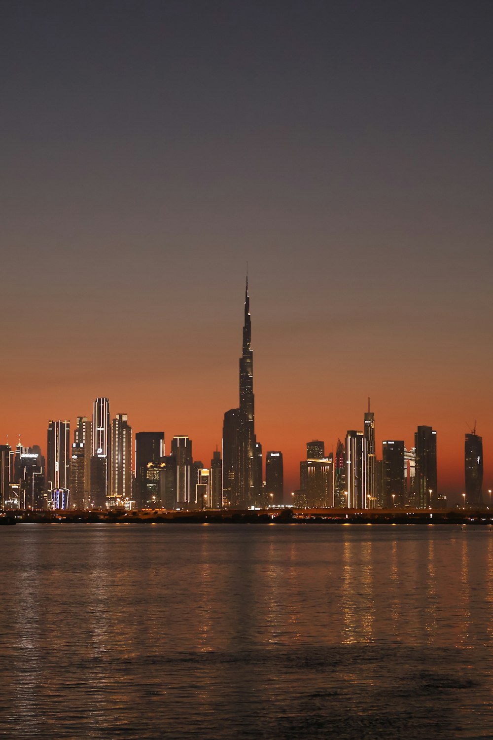 a city skyline at night with a body of water in front of it