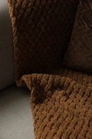 Close-up of a knitted throw blanket draped over a leather armchair beside a stone fireplace