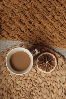 Freshly brewed coffee in a ceramic cup next to a cozy knitted blanket on a windowsill.