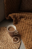 A cozy, sunlit corner with a textured throw blanket and a ceramic mug on a wooden side table.