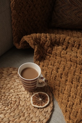 A cozy, sunlit corner with a textured throw blanket and a ceramic mug on a wooden side table.