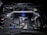 A detailed view of a high-performance car engine, featuring various components such as pipes, valves, and a distinct metallic support bar across the top. The engine has a polished look with elements in black, blue, and silver. Various branding and labels are visible on different parts.