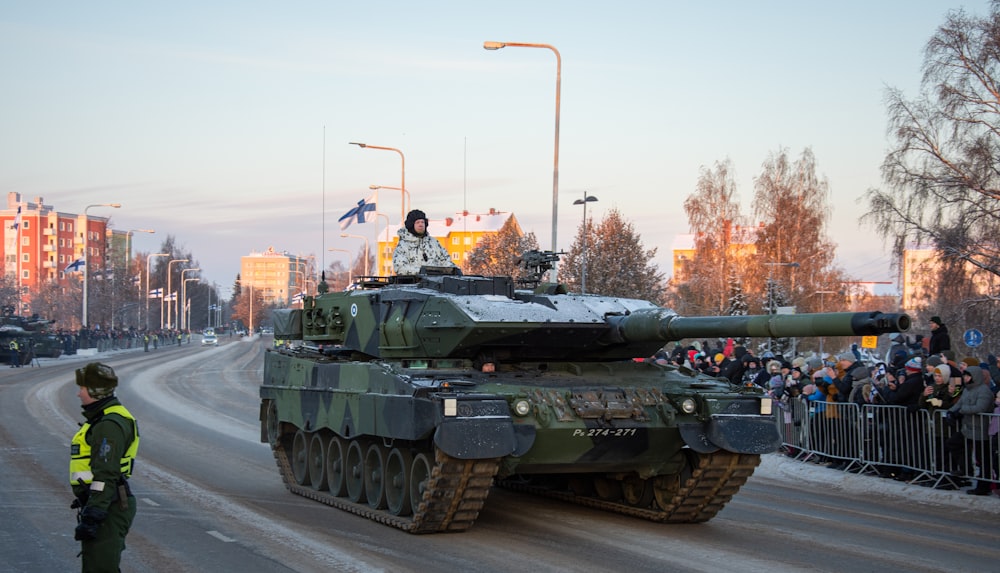 a military tank driving down a street next to a crowd of people