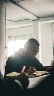 A quiet moment captured: a focused individual writing in a Kagei Exec notebook in a dimly lit room.