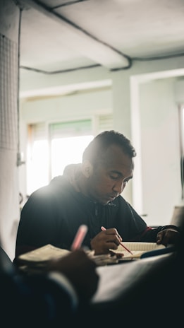 A quiet moment captured: a focused individual writing in a Kagei Exec notebook in a dimly lit room.
