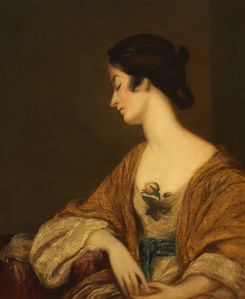 A portrait of a woman in profile, featuring a delicate and contemplative expression. Her dark hair is styled elegantly, and she is adorned in a luxurious golden robe with intricate lace detail. A rose is depicted on the fabric near her chest, adding a touch of natural beauty. The background is a muted, warm brown, highlighting the softness of her skin and the richness of her attire.