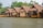 A row of traditional wooden huts built on stilts over water, featuring thatched roofs and bamboo structures. The huts are surrounded by lush greenery, including trees and plants, creating a serene and natural environment.