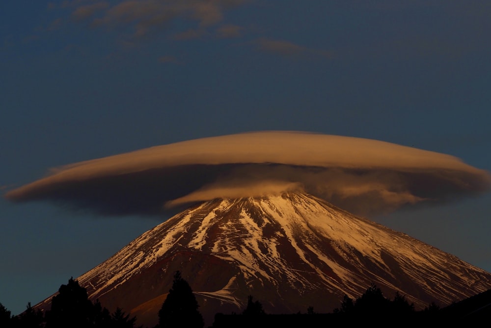 a large cloud looms over a snow covered mountain