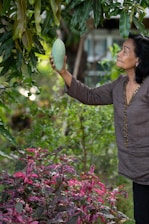 a woman holding a green fruit up to a tree