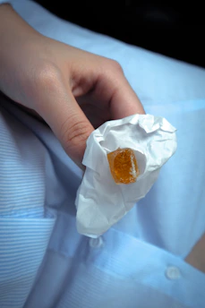 Close-up of a hand holding a soft, amber-colored gummy with a blurred background of a cozy bedroom.
