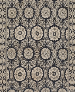 Intricate floral and geometric patterns in symmetrical arrangements dominate the textile design. Cream-colored motifs stand out against a dark background, forming a network of stylized flowers and ornate shapes. The design is bordered by a repetitive pattern of similar motifs.