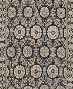 Intricate floral and geometric patterns in symmetrical arrangements dominate the textile design. Cream-colored motifs stand out against a dark background, forming a network of stylized flowers and ornate shapes. The design is bordered by a repetitive pattern of similar motifs.