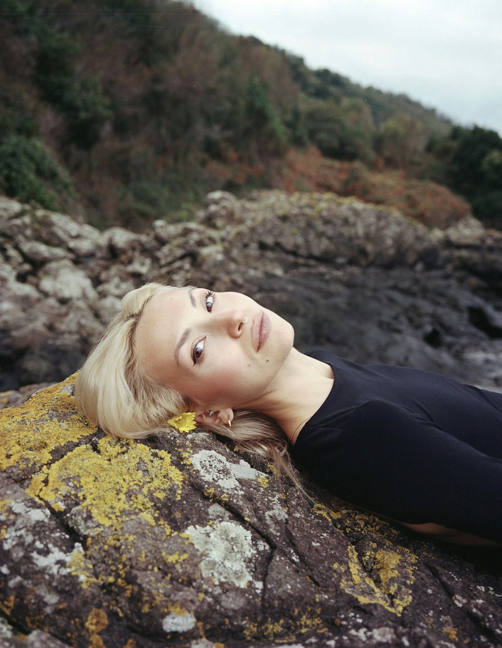 a woman laying on top of a rock next to a river