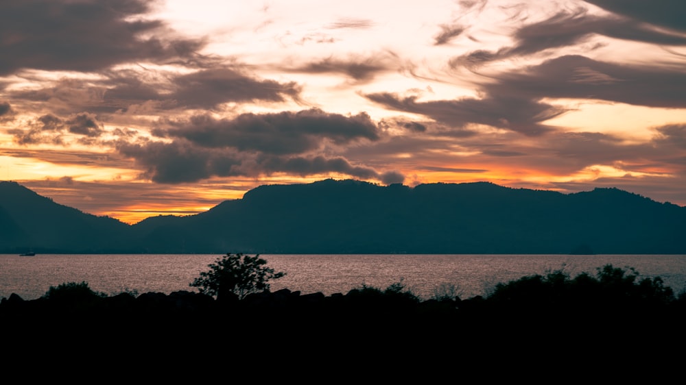 a sunset over a body of water with mountains in the background