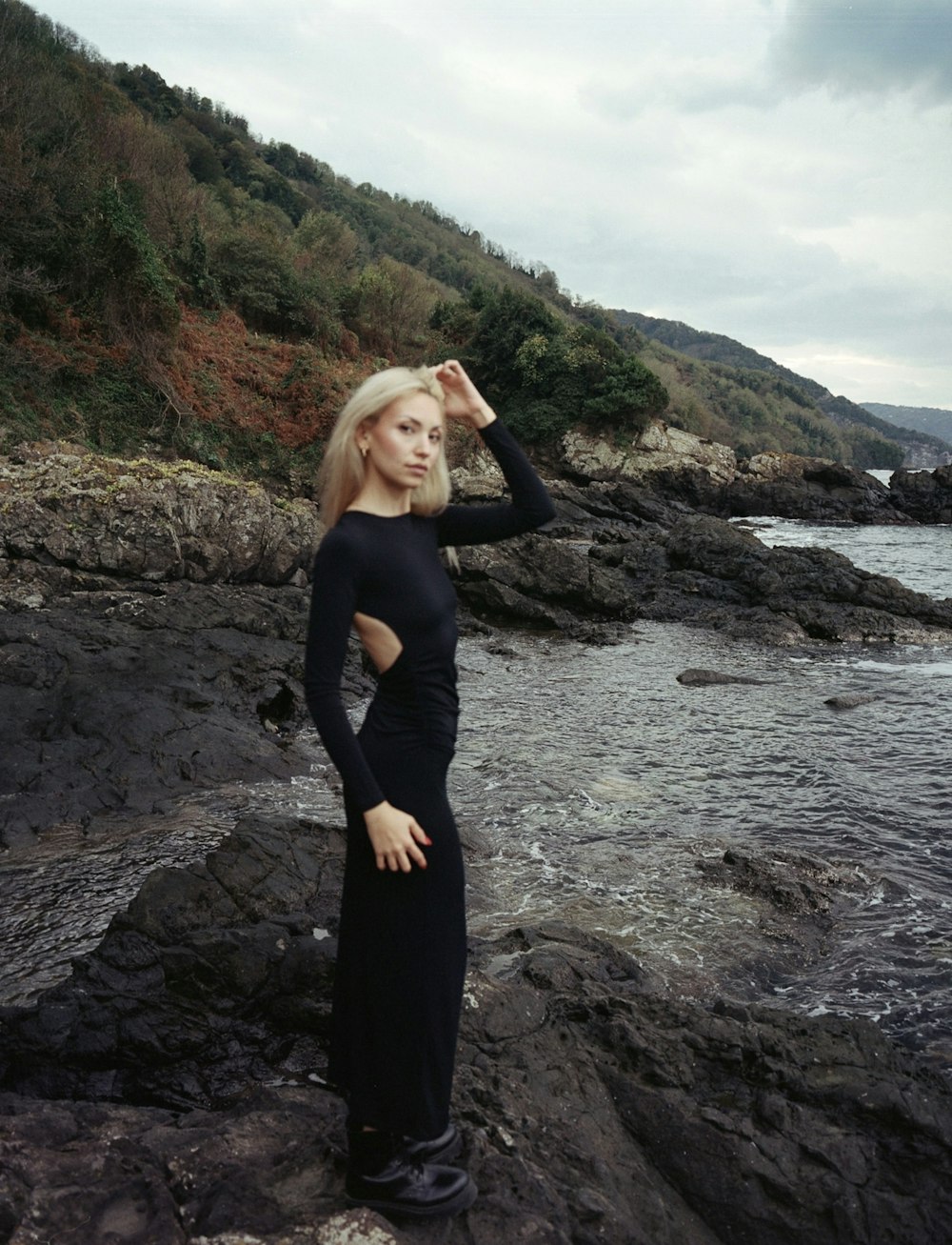 uma mulher em pé em uma costa rochosa ao lado do oceano