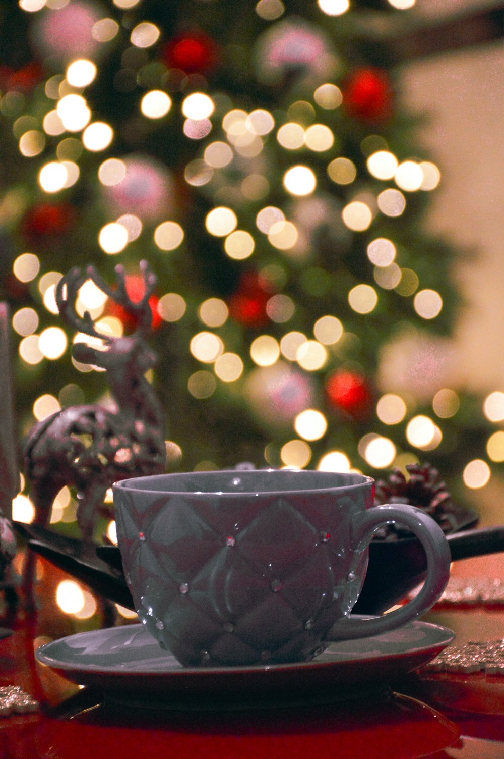 a cup and saucer on a table with a christmas tree in the background